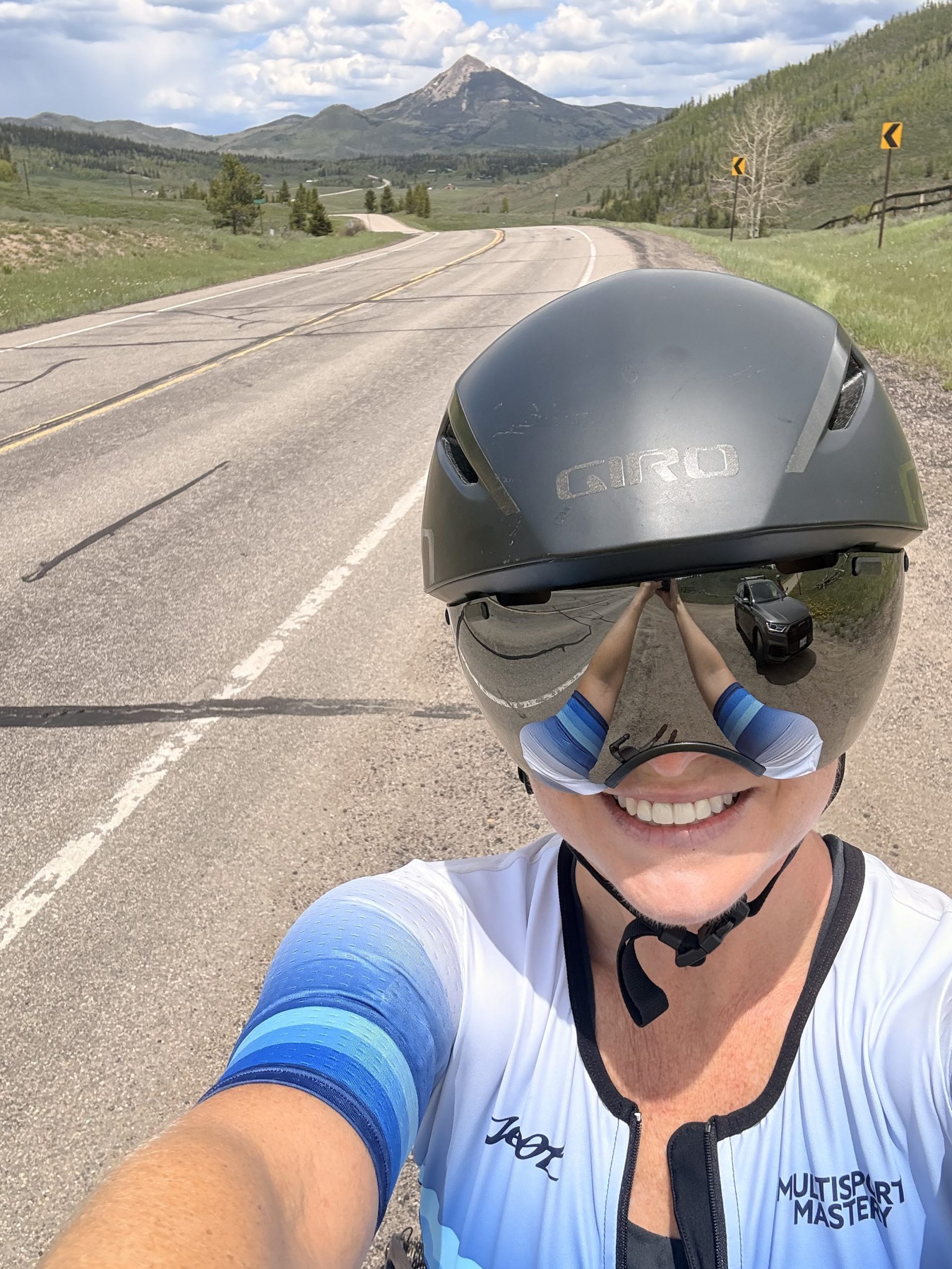 Triathlete in an aero helmet smiling on a mountain training ride, showing consistency in endurance training