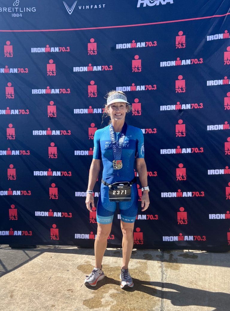 Emily wearing her finisher medal in front of an IRONMAN 70.3 backdrop