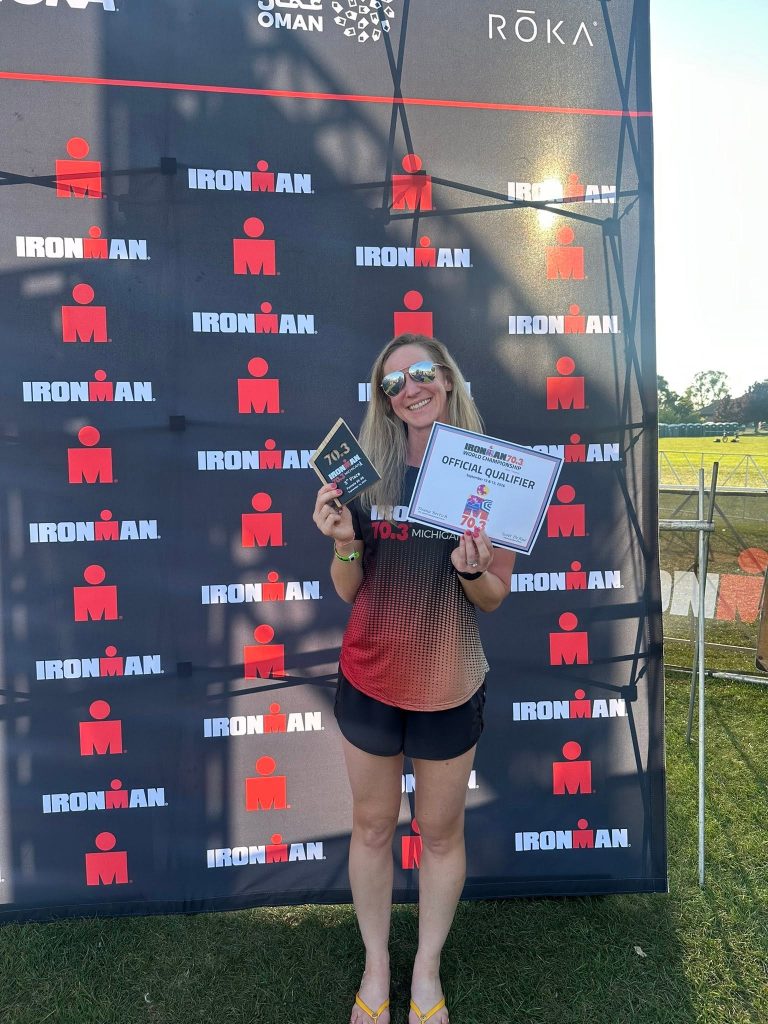 Lauren holding her finisher certificate in front of an IRONMAN backdrop