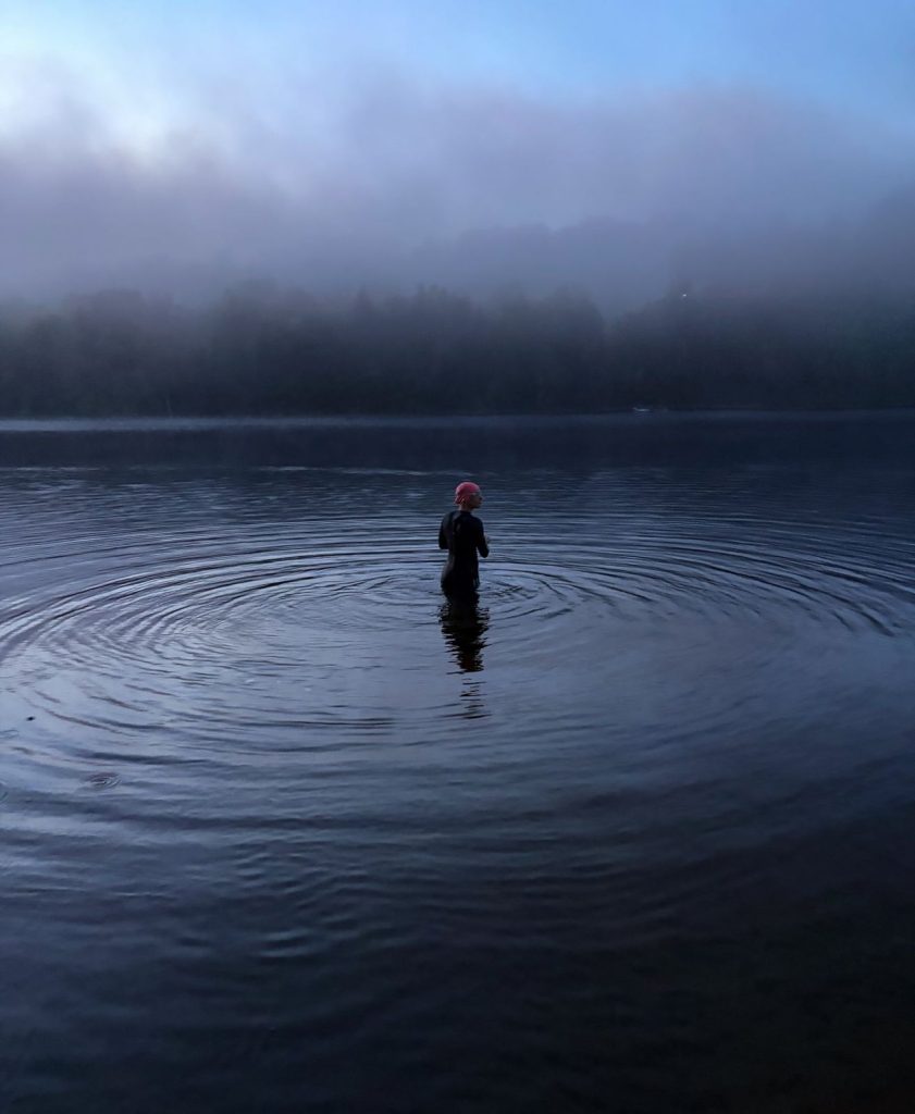 Swimmer in a pink cap wading into a misty lake at dawn