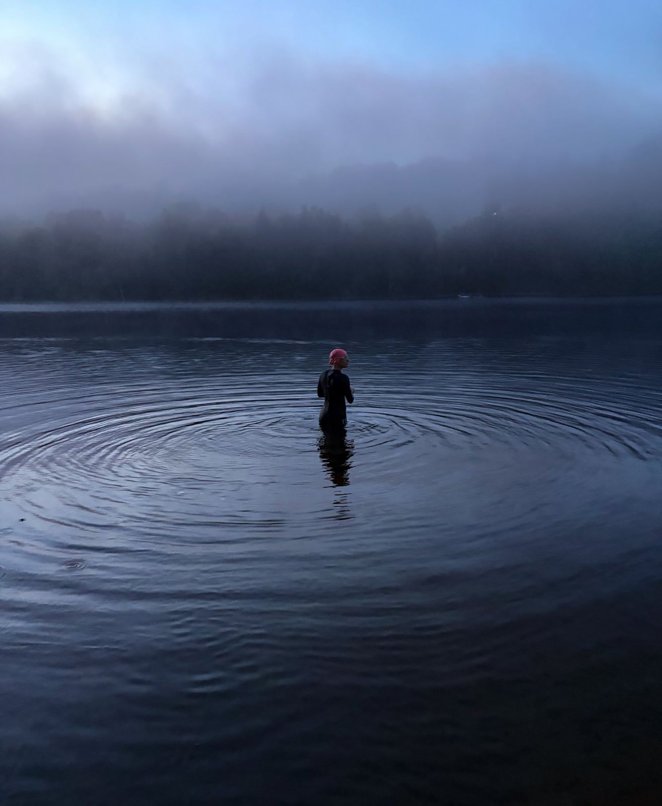 Swimmer in a pink cap wading into a misty lake at dawn
