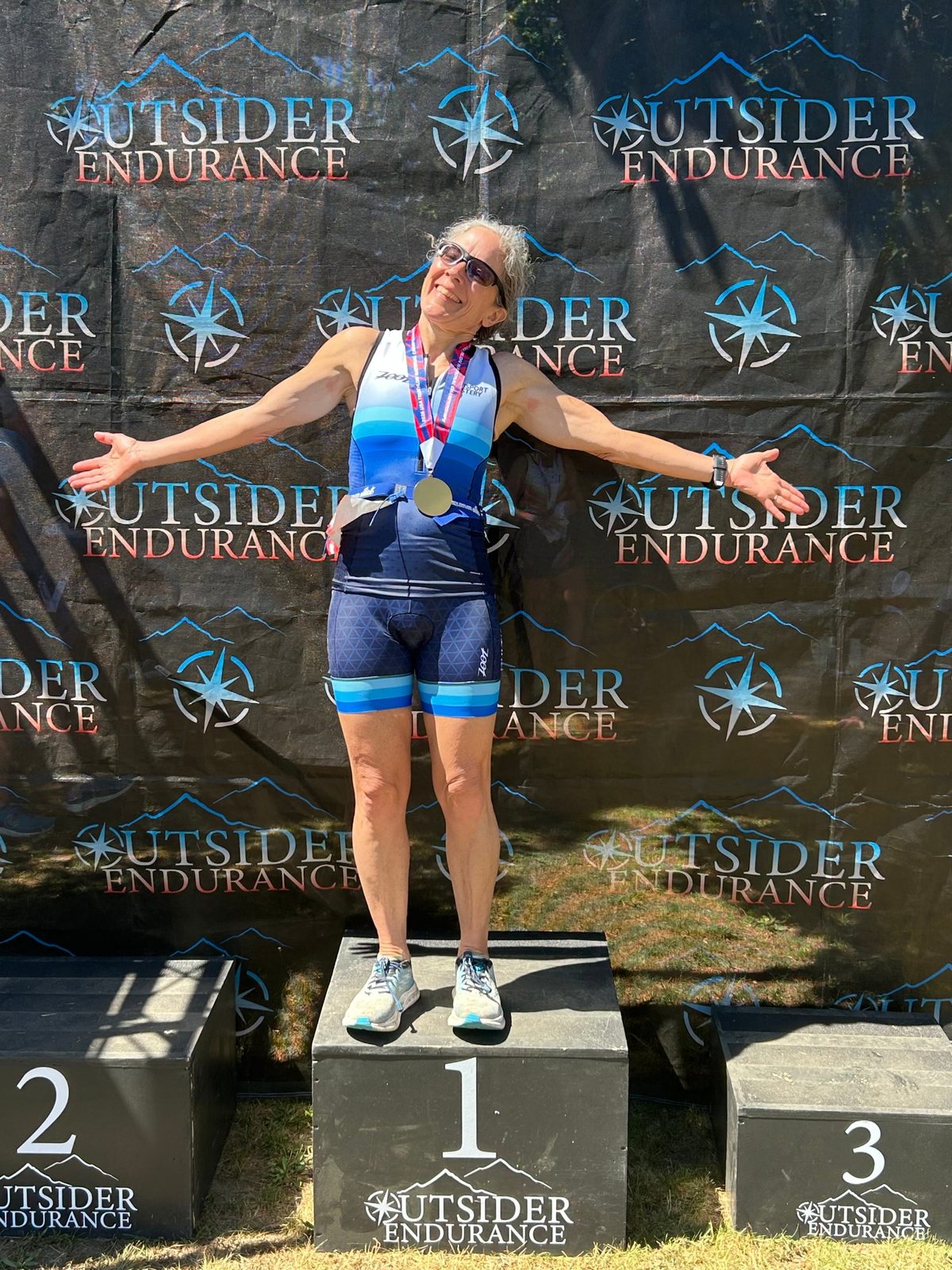 Multisport Mastery athlete on the first-place podium with her arms spread wide
