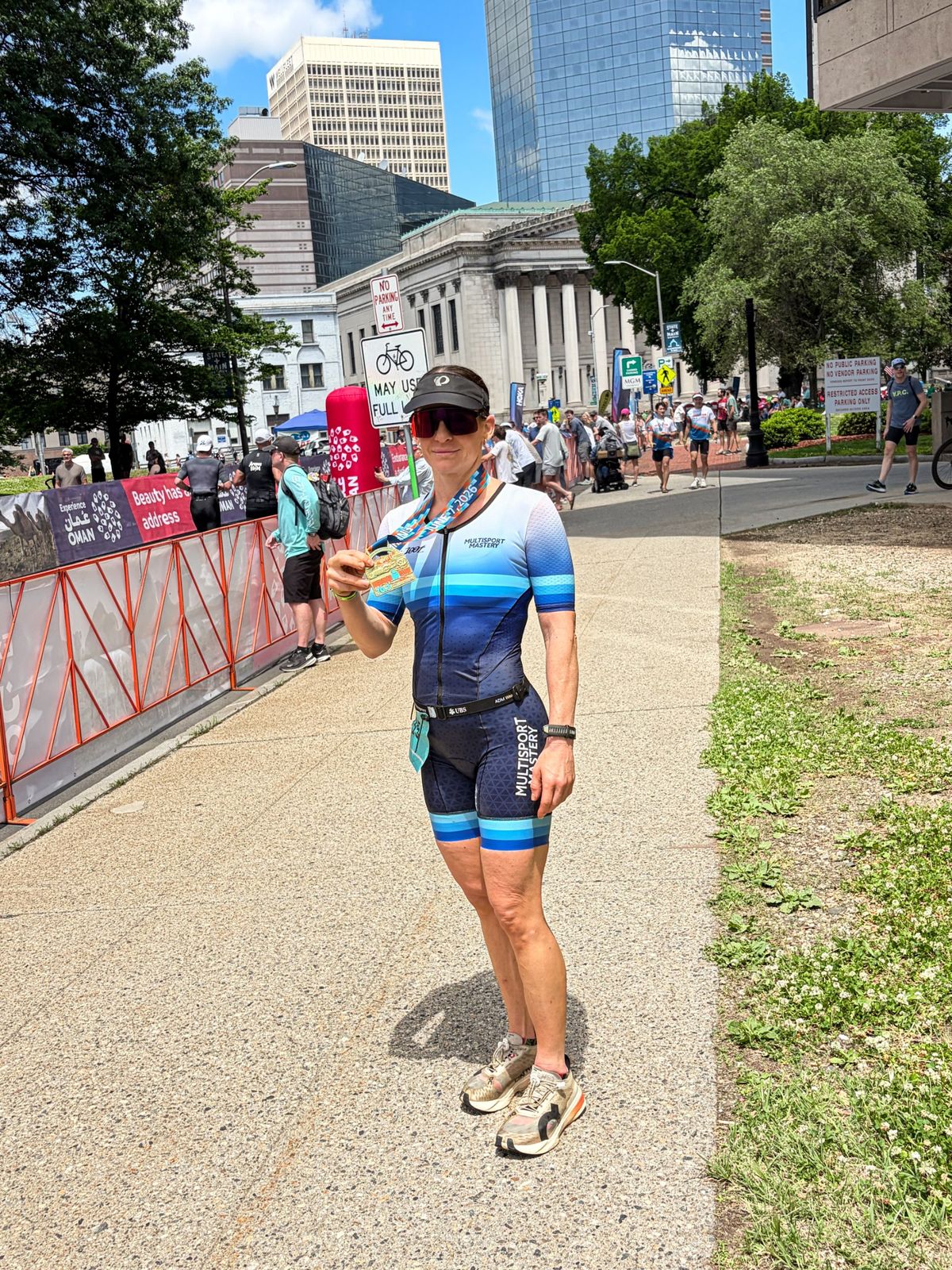 Triathlete in a Multisport Mastery kit holding up her finisher medal after a city race