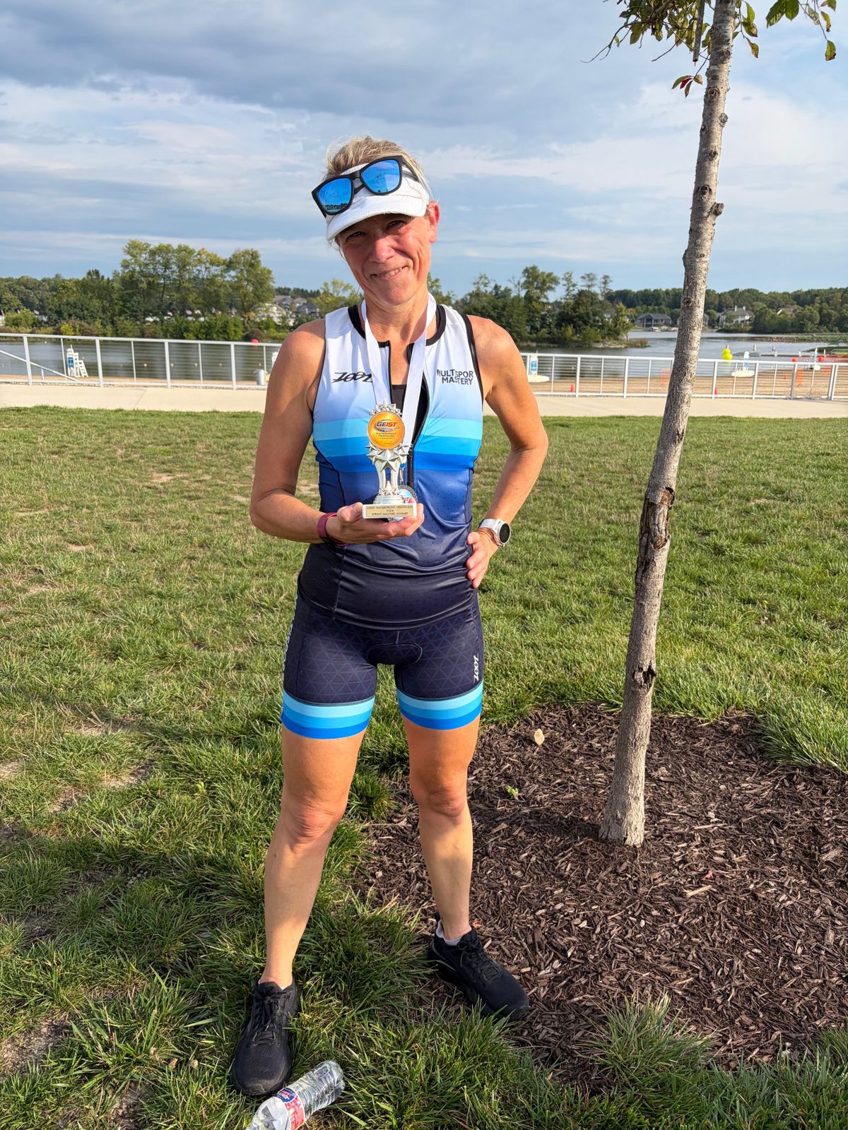 Masters triathlon winner holding her trophy beside the lake