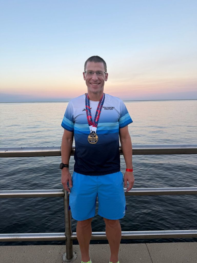 Athlete wearing his USA Triathlon Nationals first-place medal by the lake at sunset