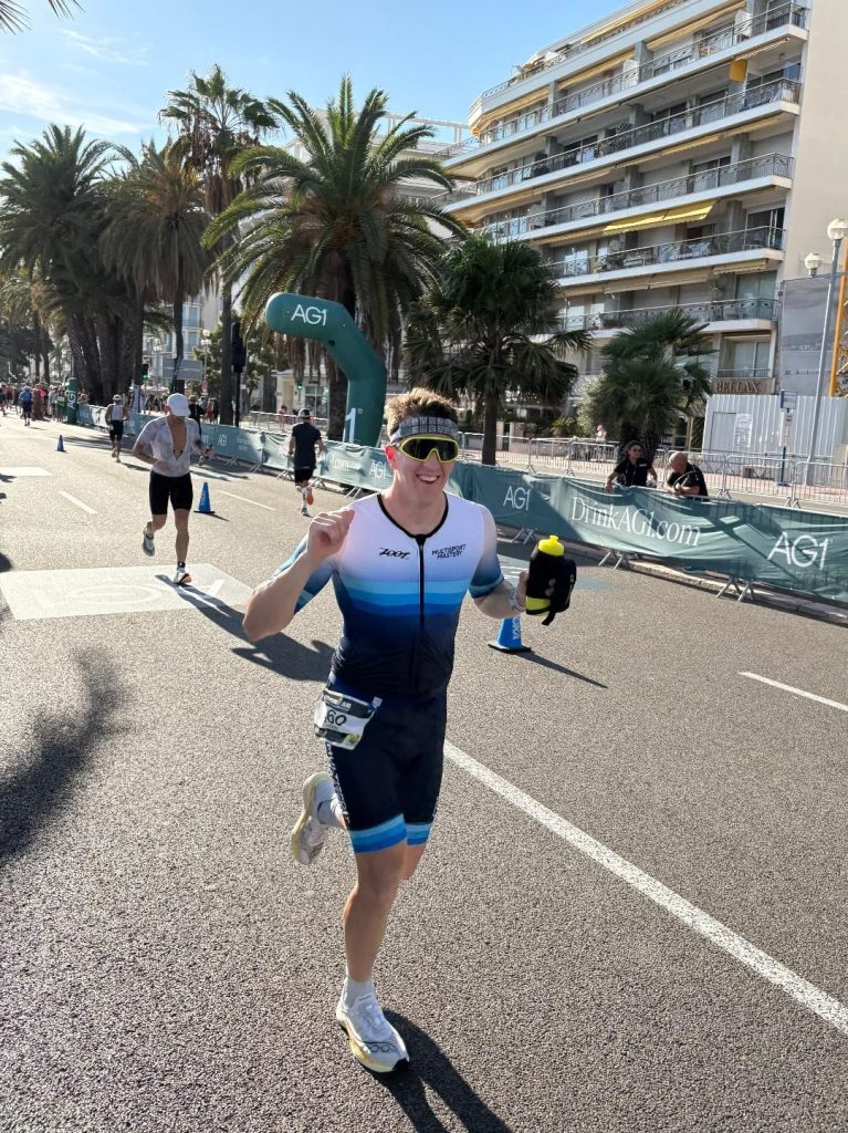 Smiling triathlete in a Multisport Mastery kit running along the waterfront in Nice
