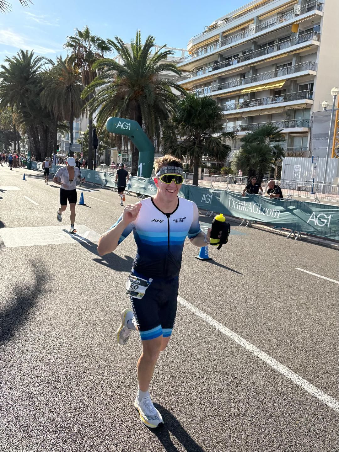 Smiling triathlete in a Multisport Mastery kit running along the waterfront in Nice
