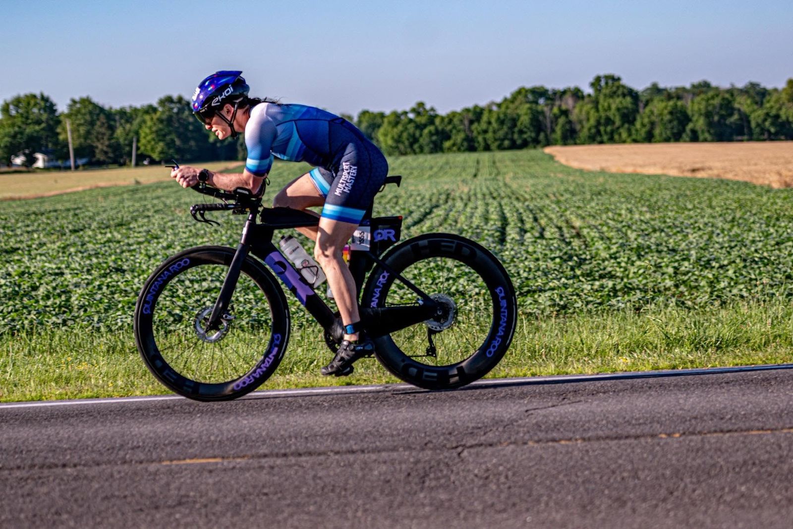 Triathlete riding a time trial bike in the aero position past farm fields