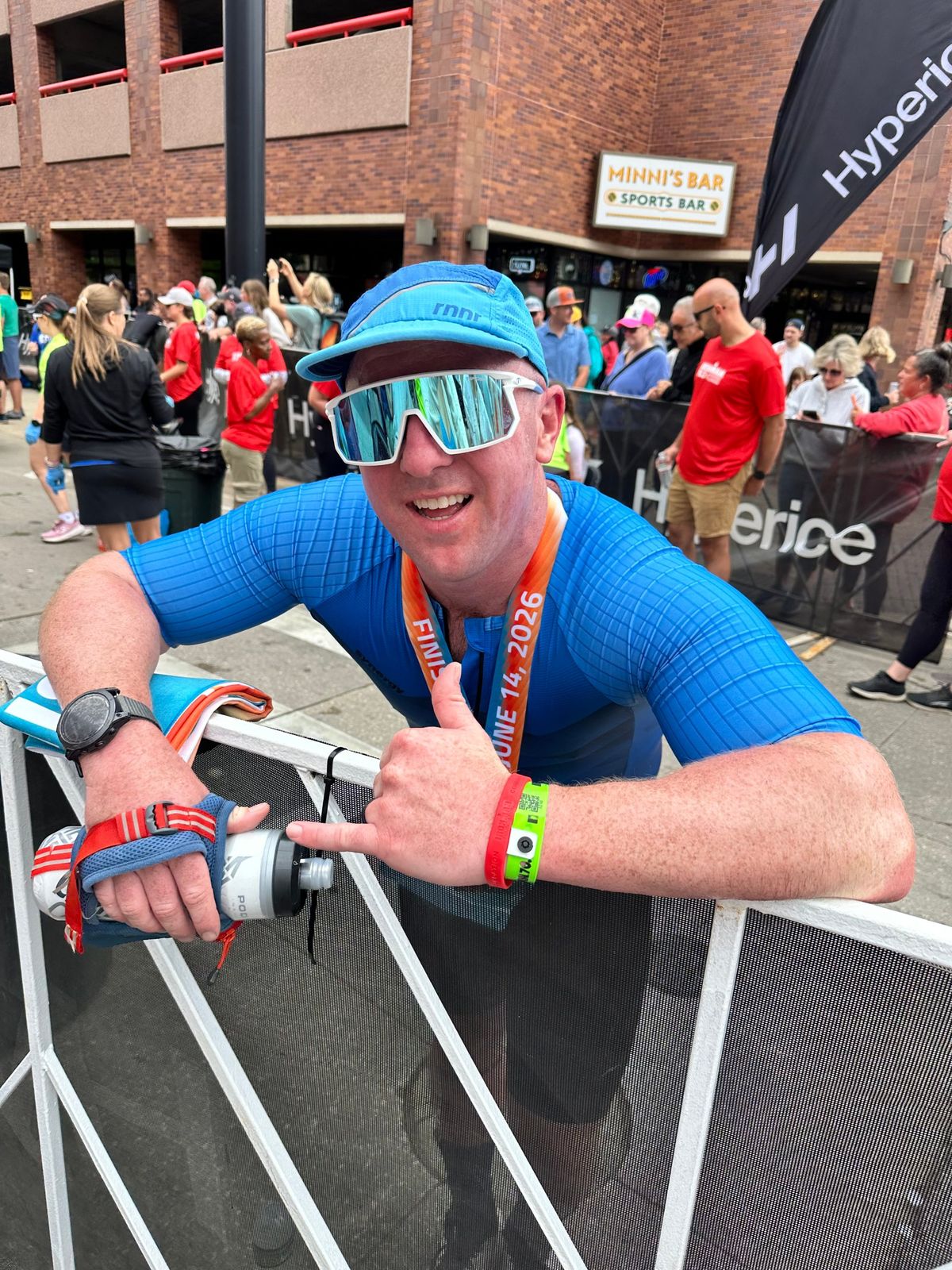 Smiling IRONMAN finisher in a blue race kit giving a thumbs up with his medal